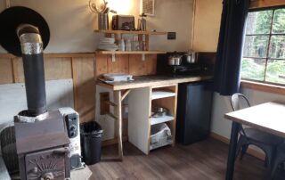 cabin 1 inside view of the kitchen, woodstove and small table and chair.