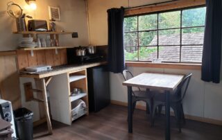 cabin 1 inside view of the kitchen, woodstove and small table and chair.